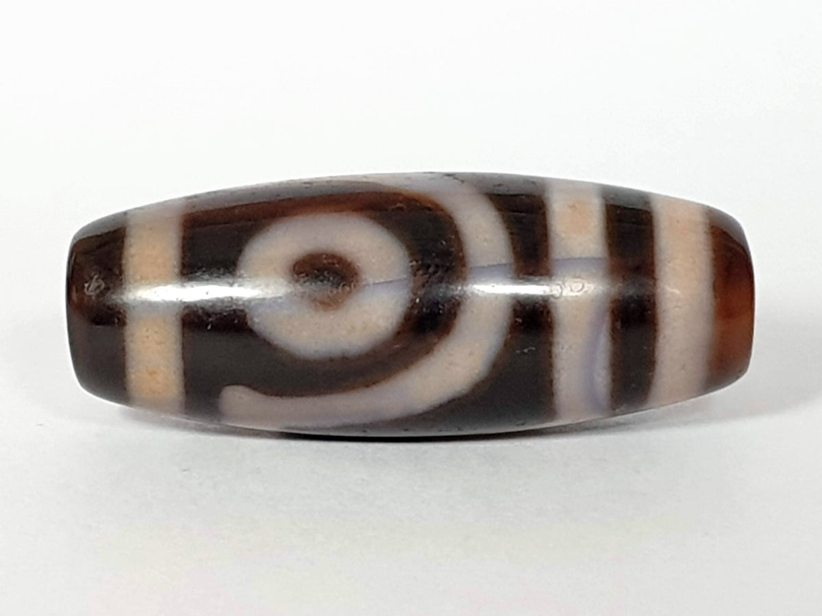 Antique carnelian dzi bead with eye spiral and stripe motifs, dark brown agate patina, polished surface, elongated barrel shape