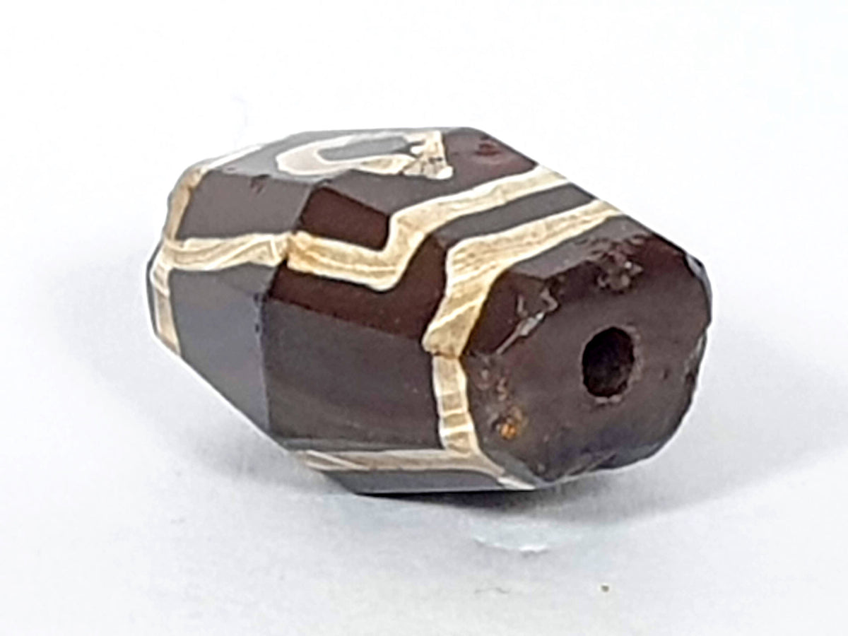 At-120120-2E7, opposite octagonal end face, ancient drilled hole, reddish oxidation, cream motif wrapping, unretouched