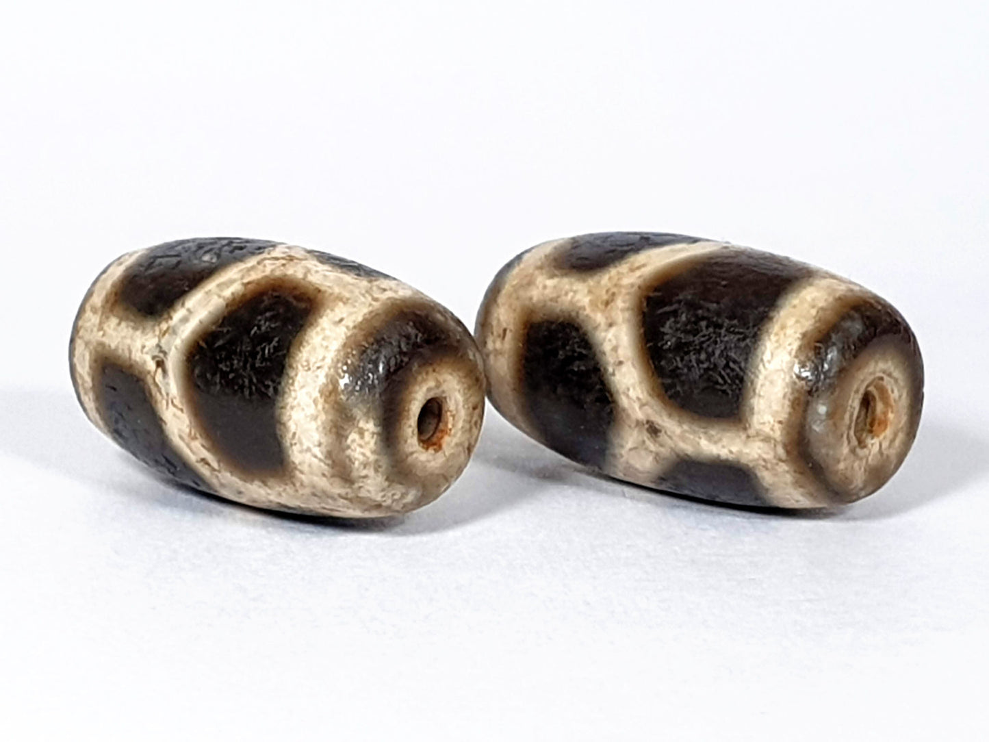 N-FA-062626-LG pair longevity dzi, angled end view, drill holes, rust-orange interiors, cream sandy ground, unretouched