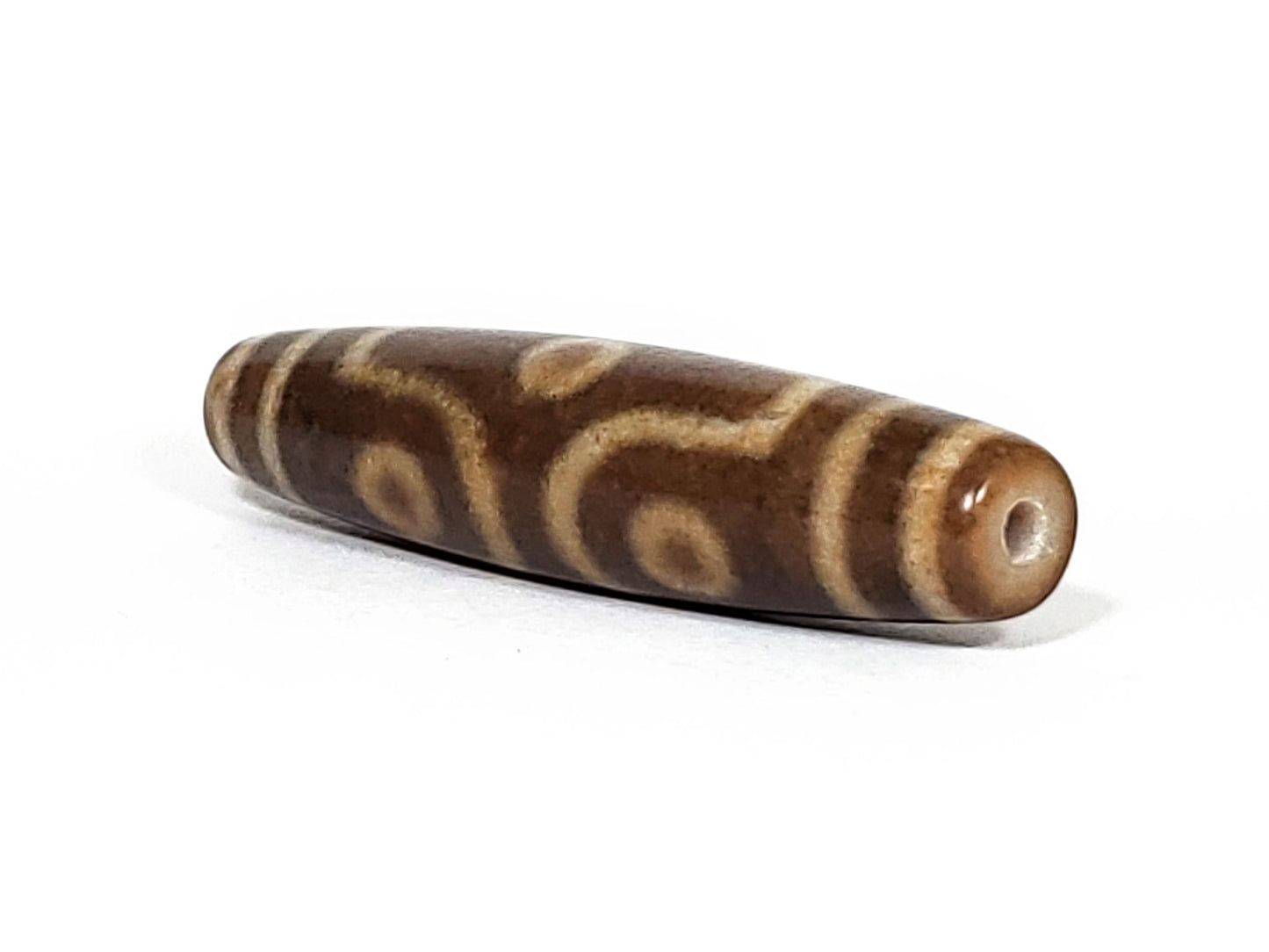 N-062226-6E2, angled toward narrow tapered tip, drill hole centred, honey-gold motif wrapping body, unretouched