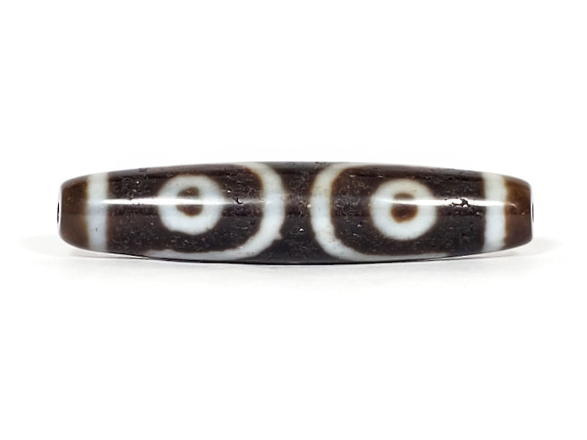 V-070226-ThE-001 dzi bead, diagonal view showing drill hole, warm brown end zone, unretouched photo.