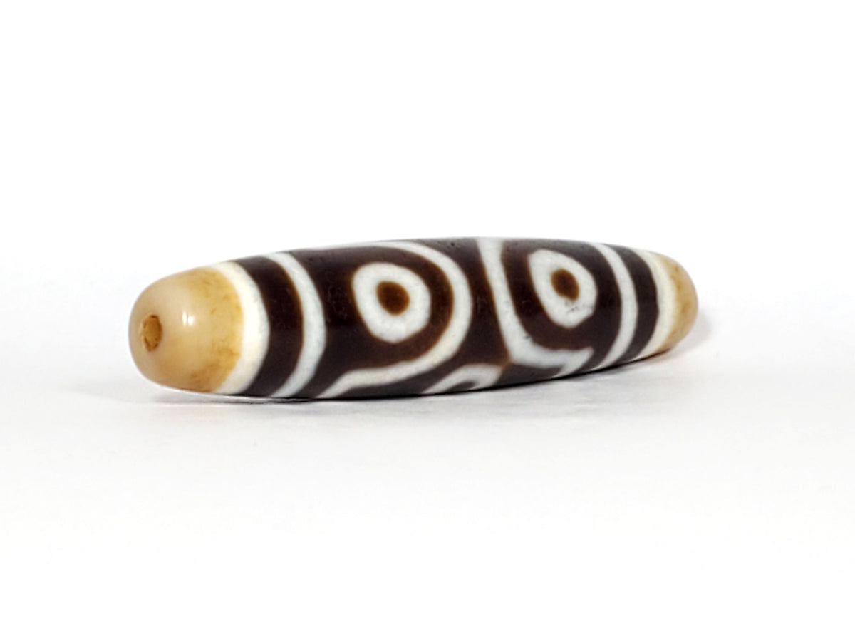 Face B of antique six eye dzi At-053026-6E, single concentric-ring eye centred in diamond star frame, cross-grid stripes, deep brown agate, honey-gold end caps, unretouched