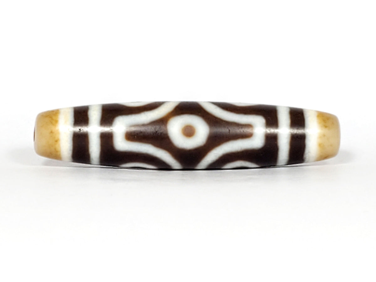Opposite end cap of antique six eye dzi At-053026-6E, warm honey-gold agate tip with drill hole, open-ring eye pair visible, full 54.9mm torpedo body, unretouched photography