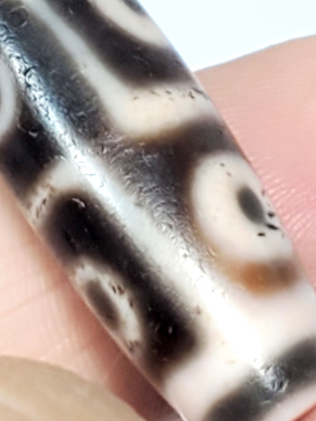 Six eye dzi bead in pale warm-brown agate with cinnabar bloodspots, held on finger showing detail and drill holes