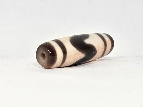 V-030326-TTBS vintage tiger tooth dzi, angled end shot, cream end cap, drill hole visible, dark motif zone, unretouched.