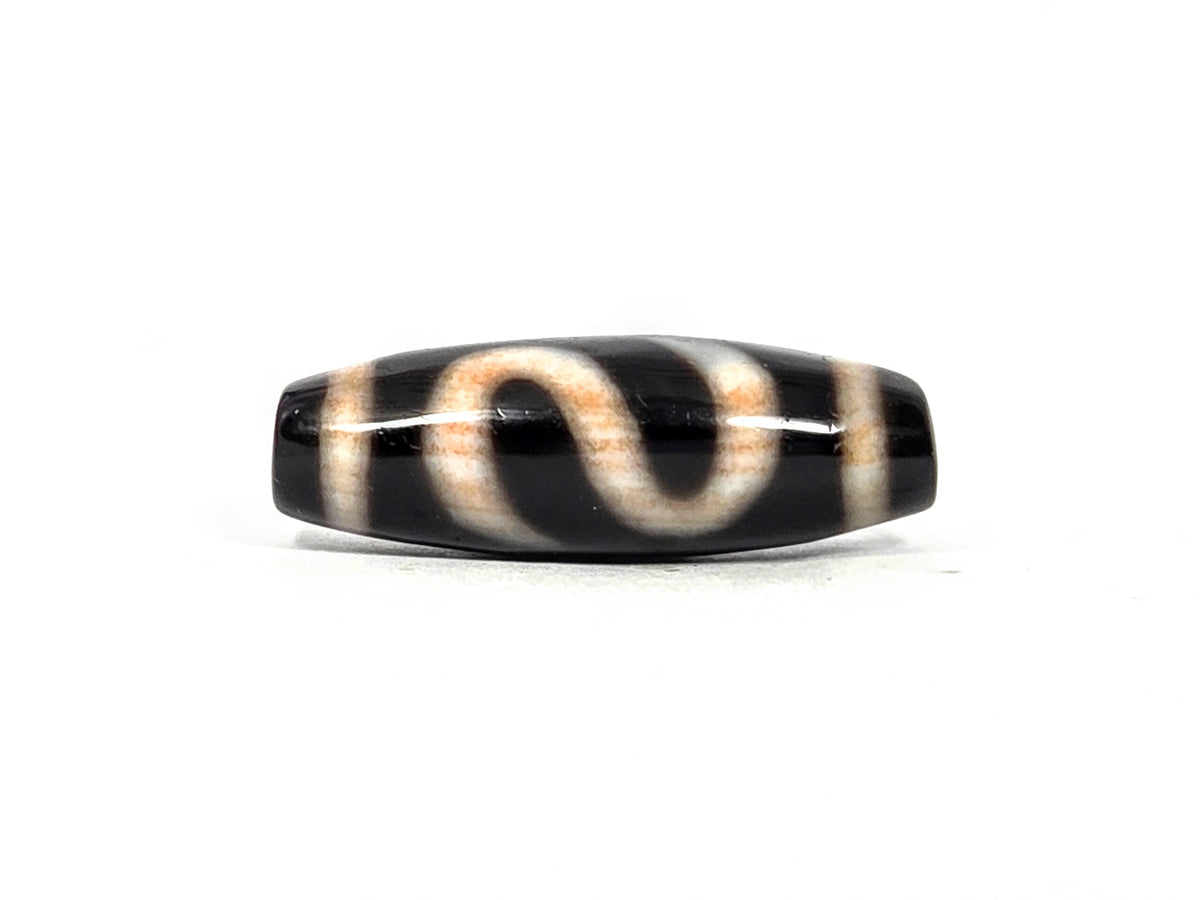 Third lateral profile of antique dzi bead AT-B-101226-MH showing full elongated barrel form, S-curve money hook motif lines, and cream-white to warm amber motif zones on deep pitch-black agate, 100–300 years old