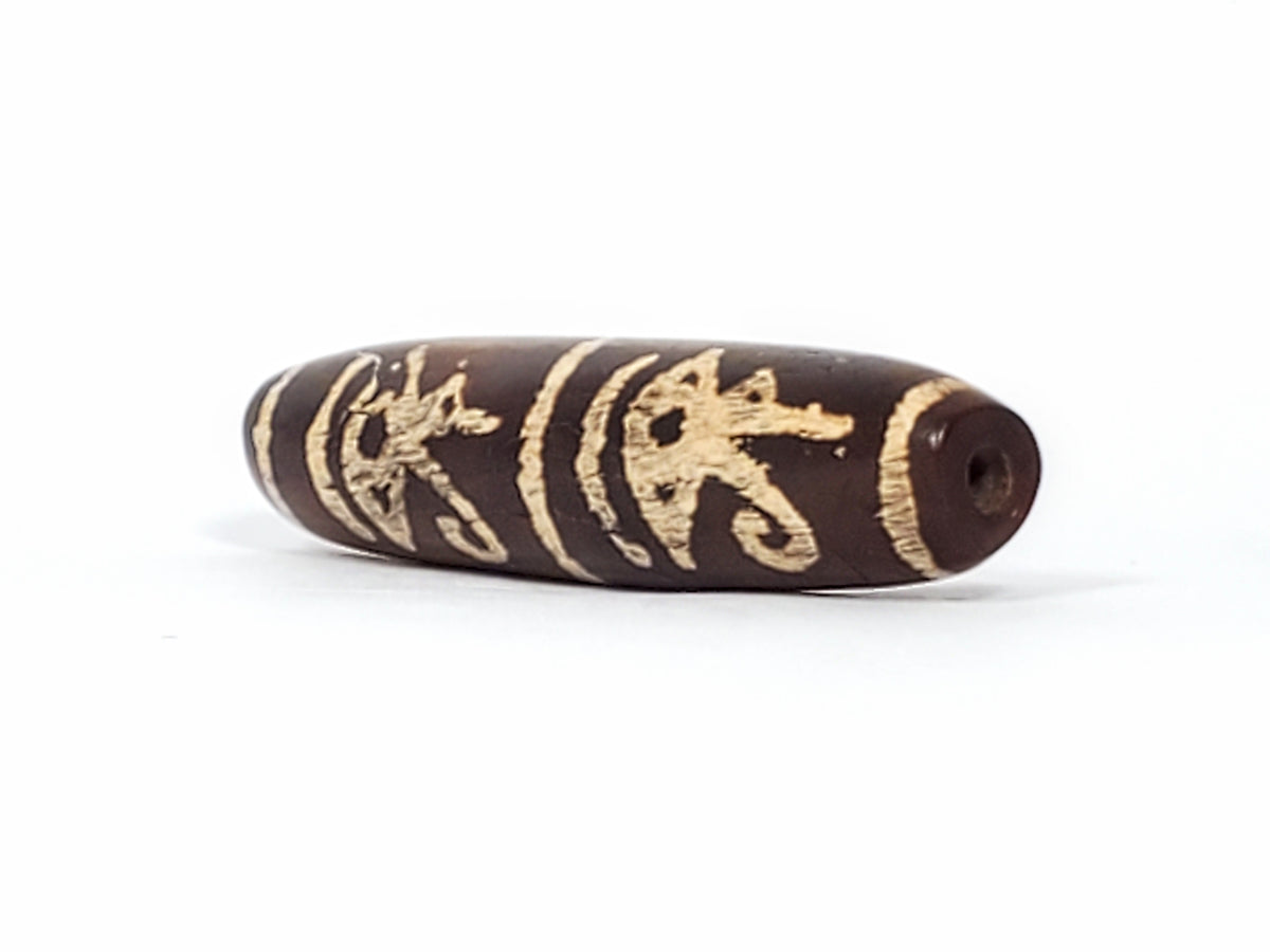 Brown dzi bead with carved gold Eye of Horus, scarab, and Ba bird motifs, visible drill hole, aged patina, elongated barrel shape