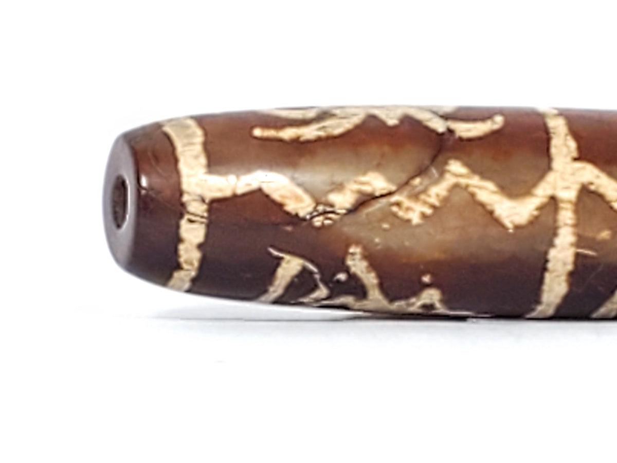 Brown agate dzi bead with cream etched zigzag wave motif pattern, visible drill hole, aged patina surface texture