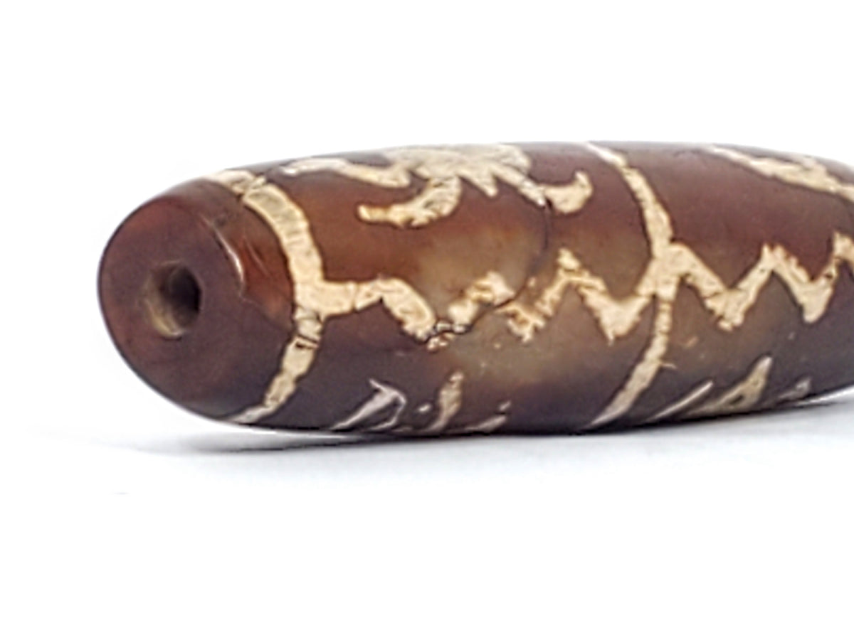Ancient etched agate dzi bead, brown with cream wave and zigzag patterns, visible drill hole, worn patina, elongated barrel shape