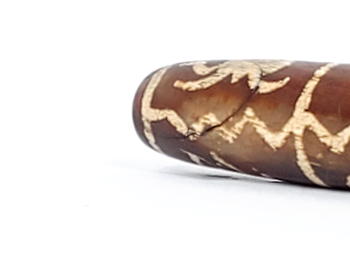 Ancient Tibetan dzi bead brown agate etched cream motifs cylindrical patina visible surface texture collectible