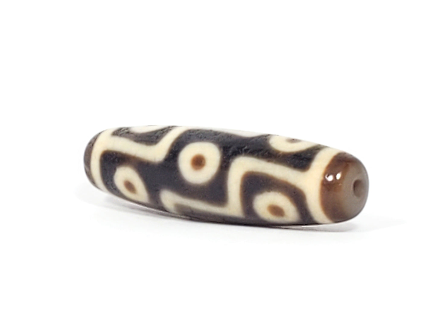 Ancient Tibetan nine-eye dzi bead, dark agate with cream eye motifs, visible drill hole, aged patina, elongated barrel shape