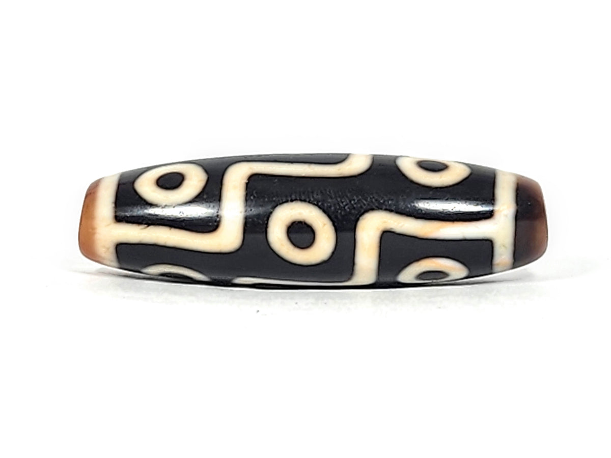Antique Tibetan nine-eye dzi bead, black agate with cream white eye motifs, wave lines, brown patina tips, elongated barrel shape