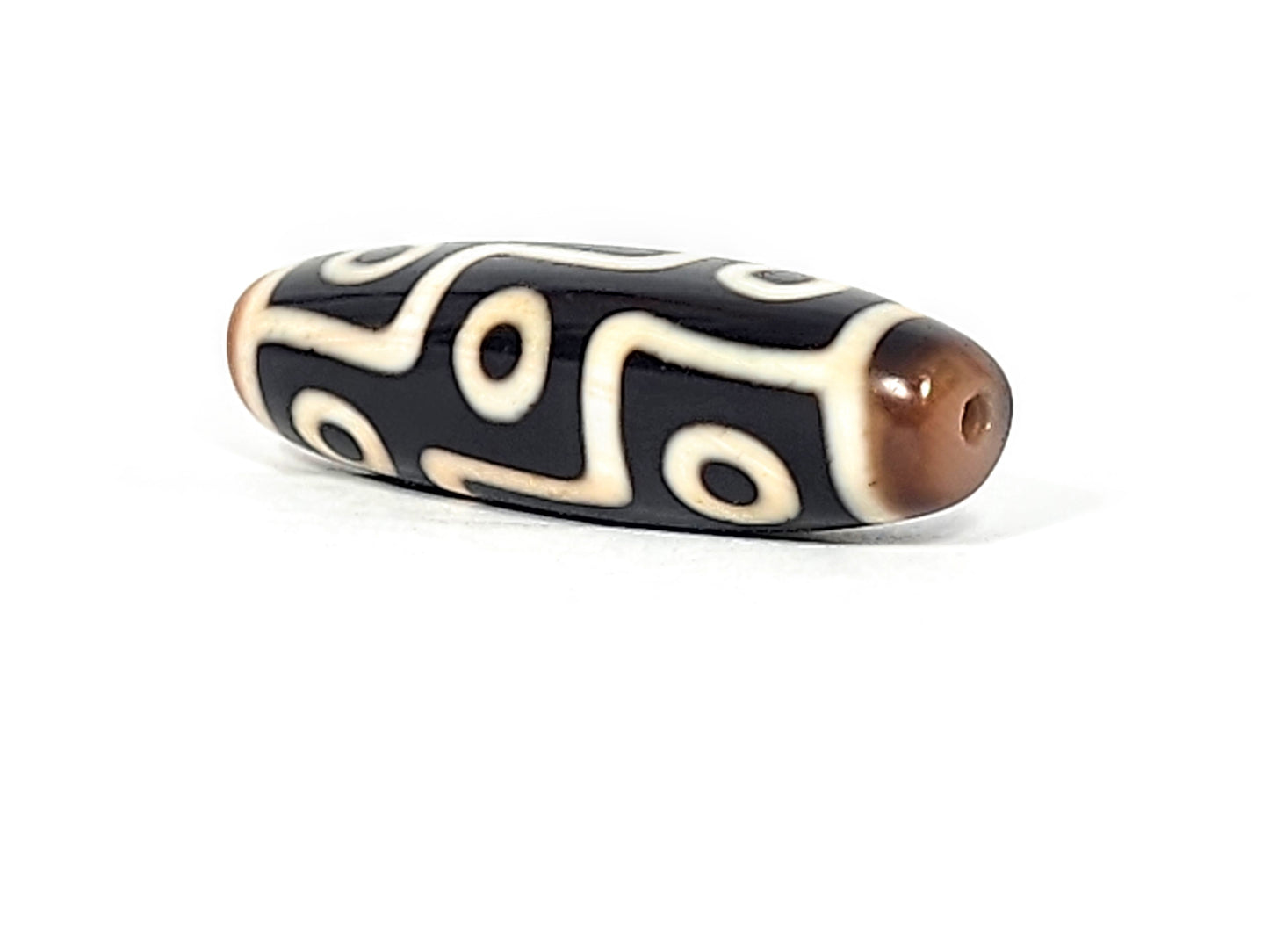Antique Tibetan nine-eye dzi bead, black agate with cream white eye motifs, brown patina tips, visible drill hole, wavy line pattern