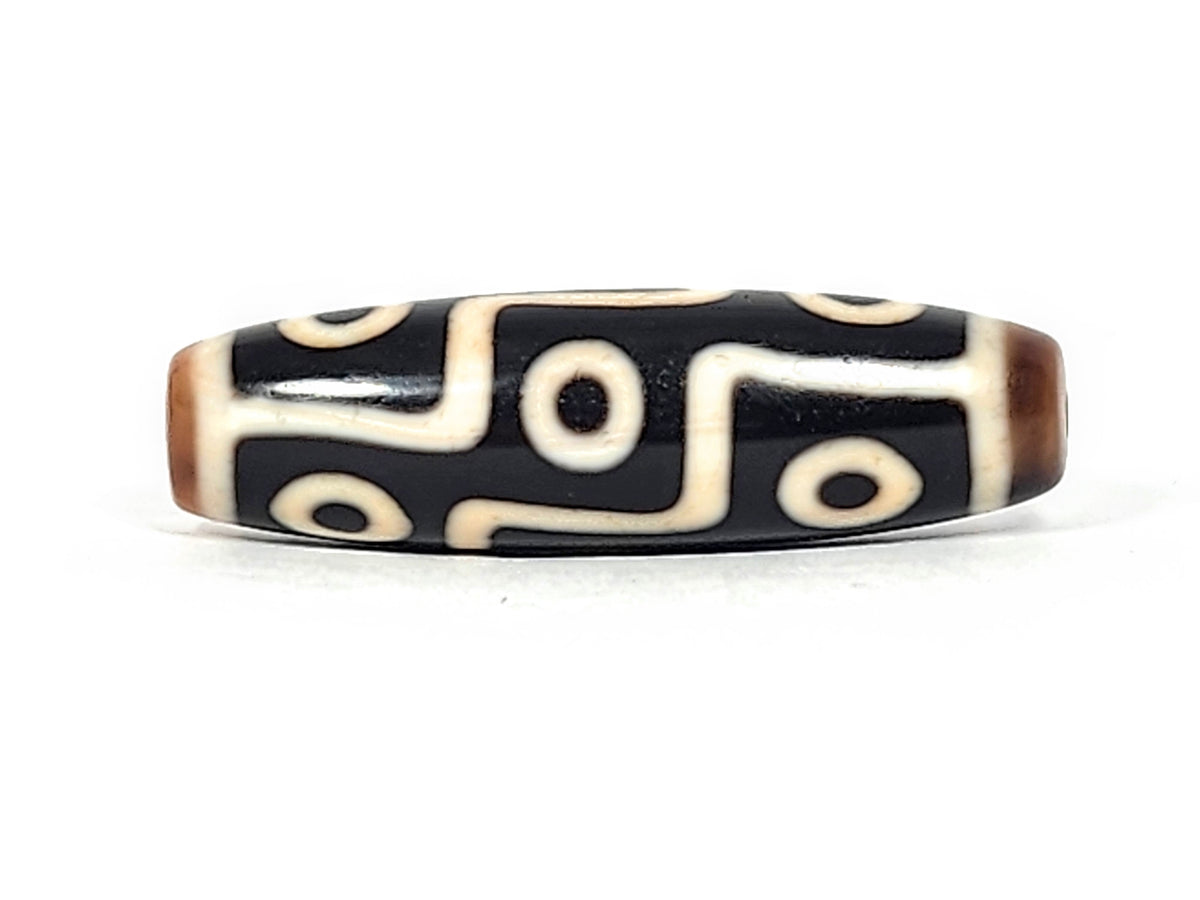 Antique Tibetan nine-eye dzi bead, black agate with cream white eye motifs and wave lines, brown patina at ends
