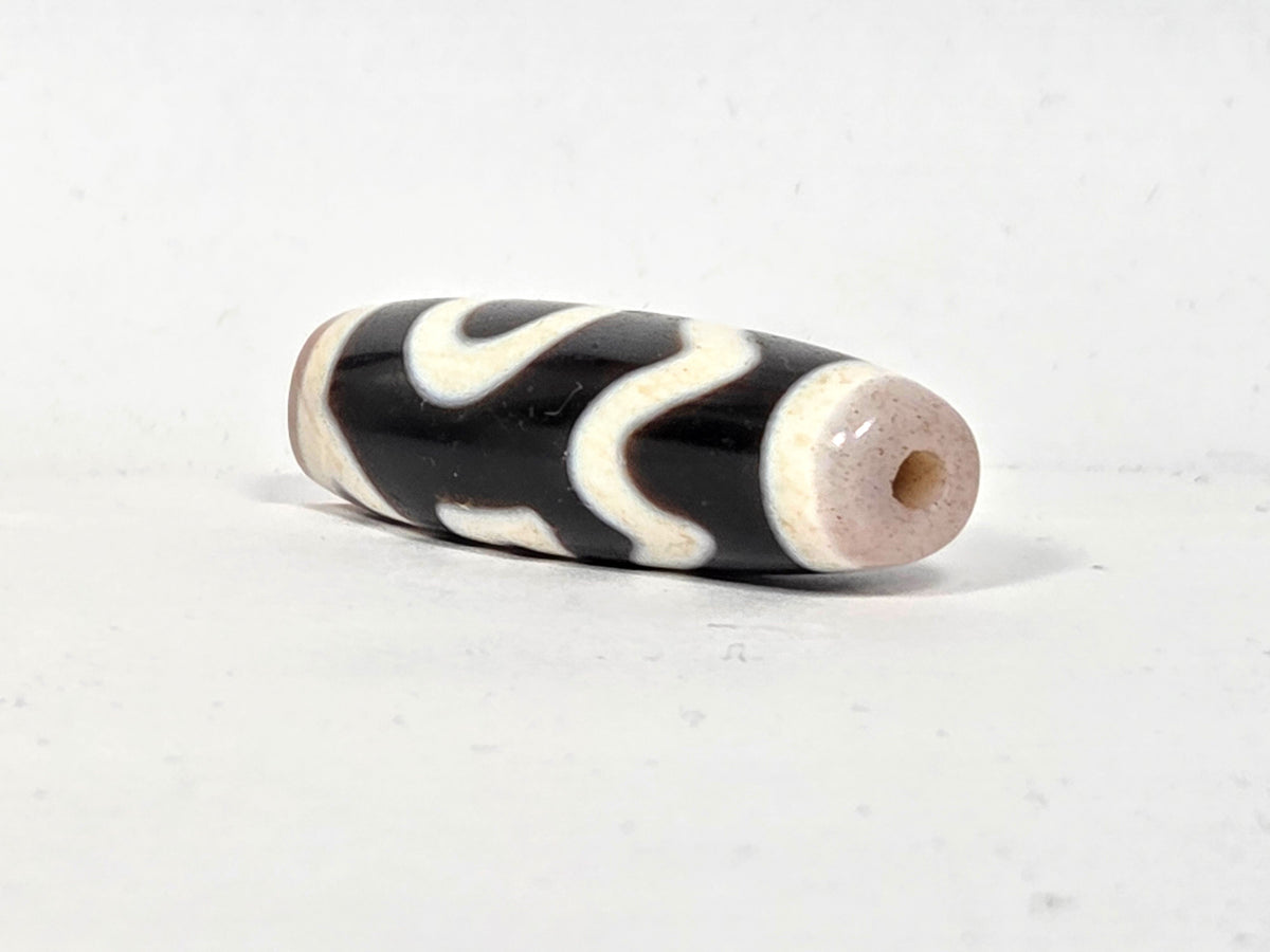 Antique Tibetan Dzi bead, four wave motif, black agate, cream etched lines, visible drill hole, aged patina, bloodspot inclusions