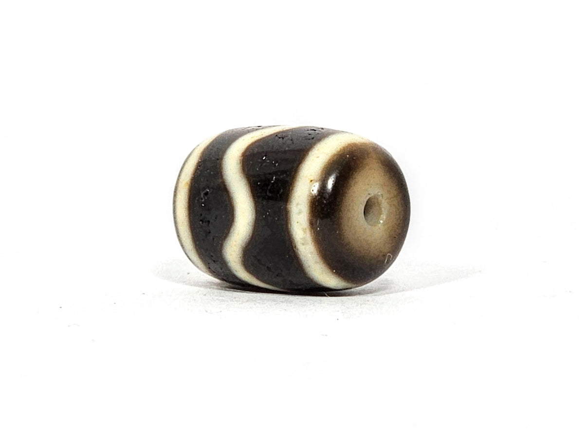 Antique wave motif dzi bead, dark brown agate with cream wavy stripes, visible drill hole, aged patina, barrel shape