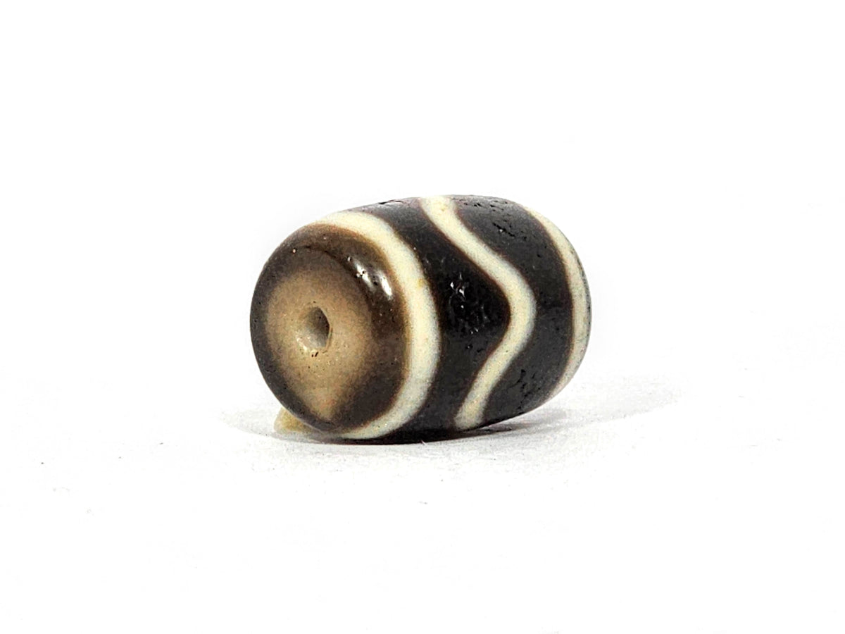 Antique wave motif dzi bead, dark agate with white wavy stripes, visible drill hole, aged patina, barrel-shaped