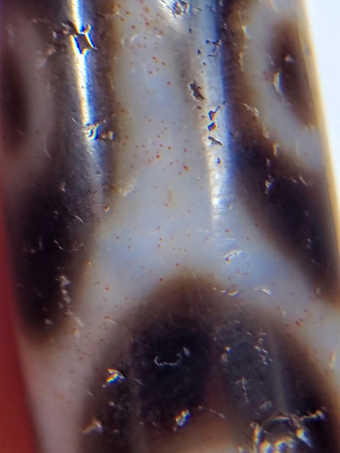 Antique Tibetan six-eye lotus dzi bead close-up showing agate surface, bloodspots, patina, and visible drill hole detail.