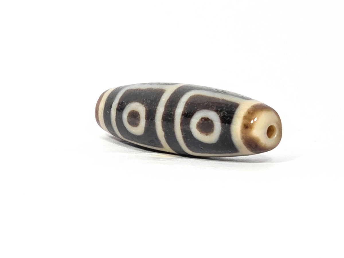 Antique Tibetan dzi bead four-eye motif dark agate white eye circles stripe pattern visible drill hole aged patina surface