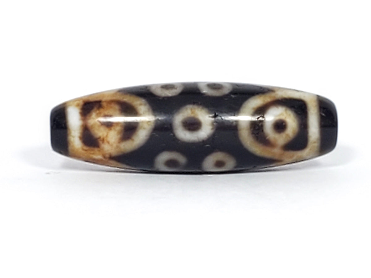 Antique Tibetan 15-eye dzi bead, black agate, white eye motifs, aged patina, oval barrel shape, natural bloodspots visible