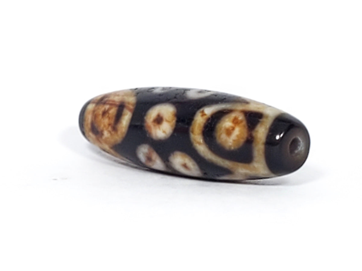 Antique Tibetan 15-eye dzi bead, dark agate, cream-brown eye motifs, natural patina, visible drill hole, elongated oval shape