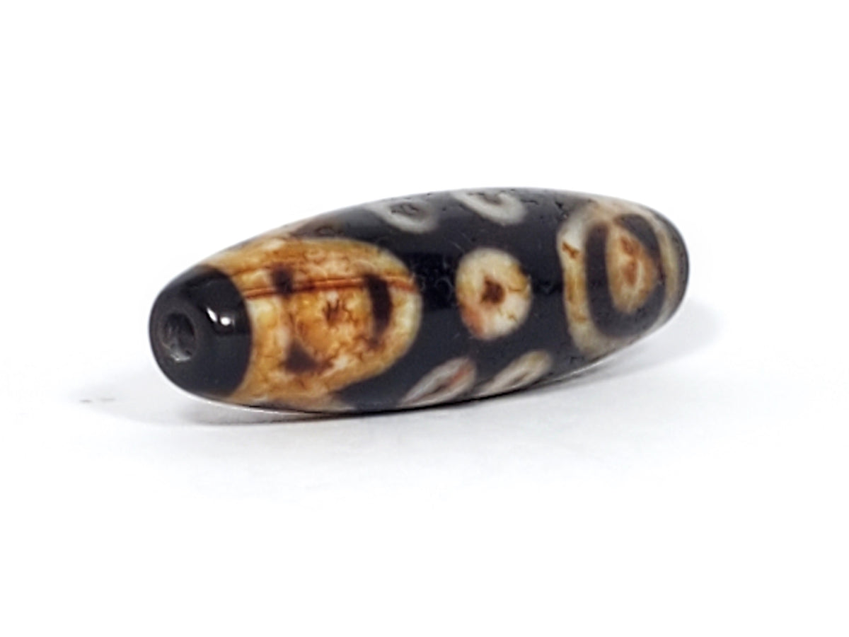 Antique Tibetan 15-eye dzi bead, black agate, cream eye motifs, natural patina, visible drill hole, elongated barrel shape