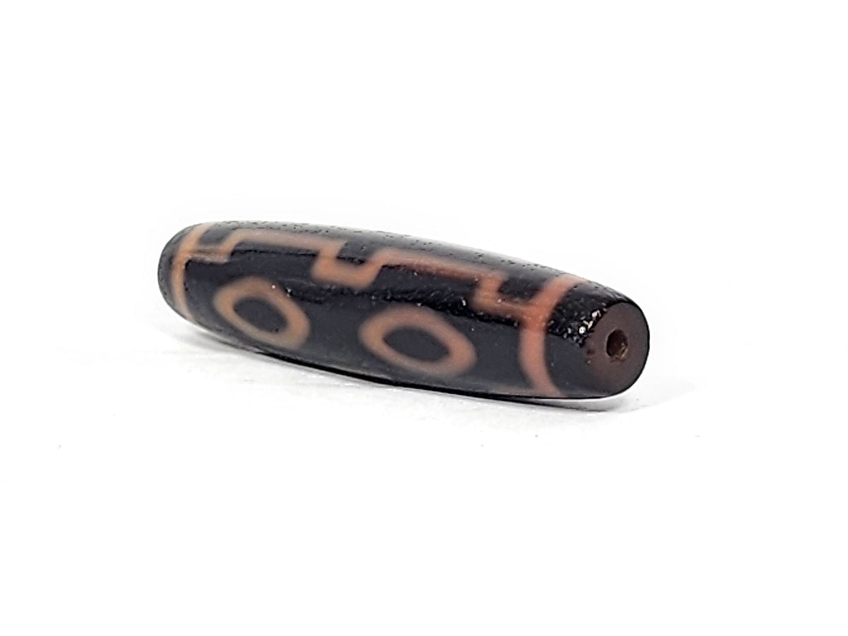 Three-quarter view of antique Four Eye dzi At-012325-4E, dark brown end cap with drill hole, amber motif lines wrapping torpedo body, 51.9mm × 12.2mm, unretouched