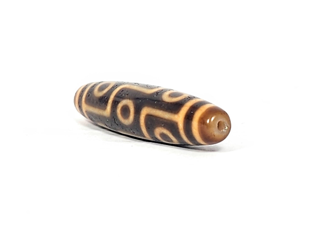 Antique Tibetan nine-eye dzi bead, dark brown agate, cream eye motifs, aged patina, visible drill hole, elongated barrel shape
