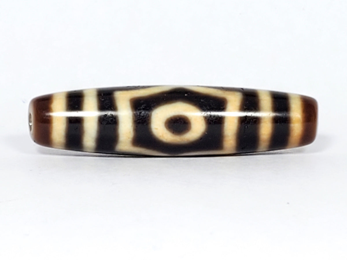 Antique Tibetan three-eye dzi bead, dark agate with cream stripes, central eye motif, visible drill hole, natural patina
