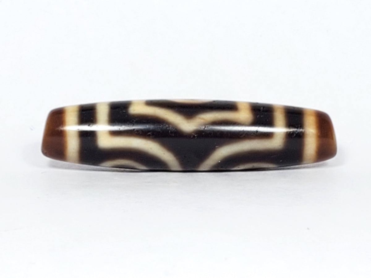 Antique three-eye dzi bead, black and cream agate, geometric motif, brown patina, elongated barrel shape, aged surface texture