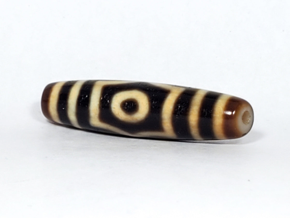 Antique Tibetan three-eye dzi bead, dark brown agate, cream stripe pattern, eye motif, visible drill hole, natural patina