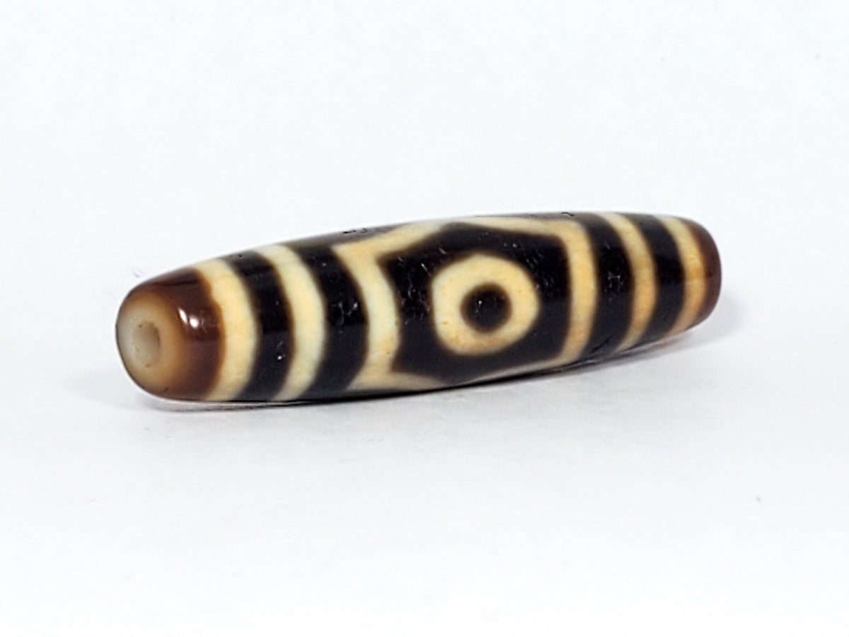 Antique three-eye dzi bead, elongated barrel agate, black and cream stripe pattern, visible drill hole, aged patina surface