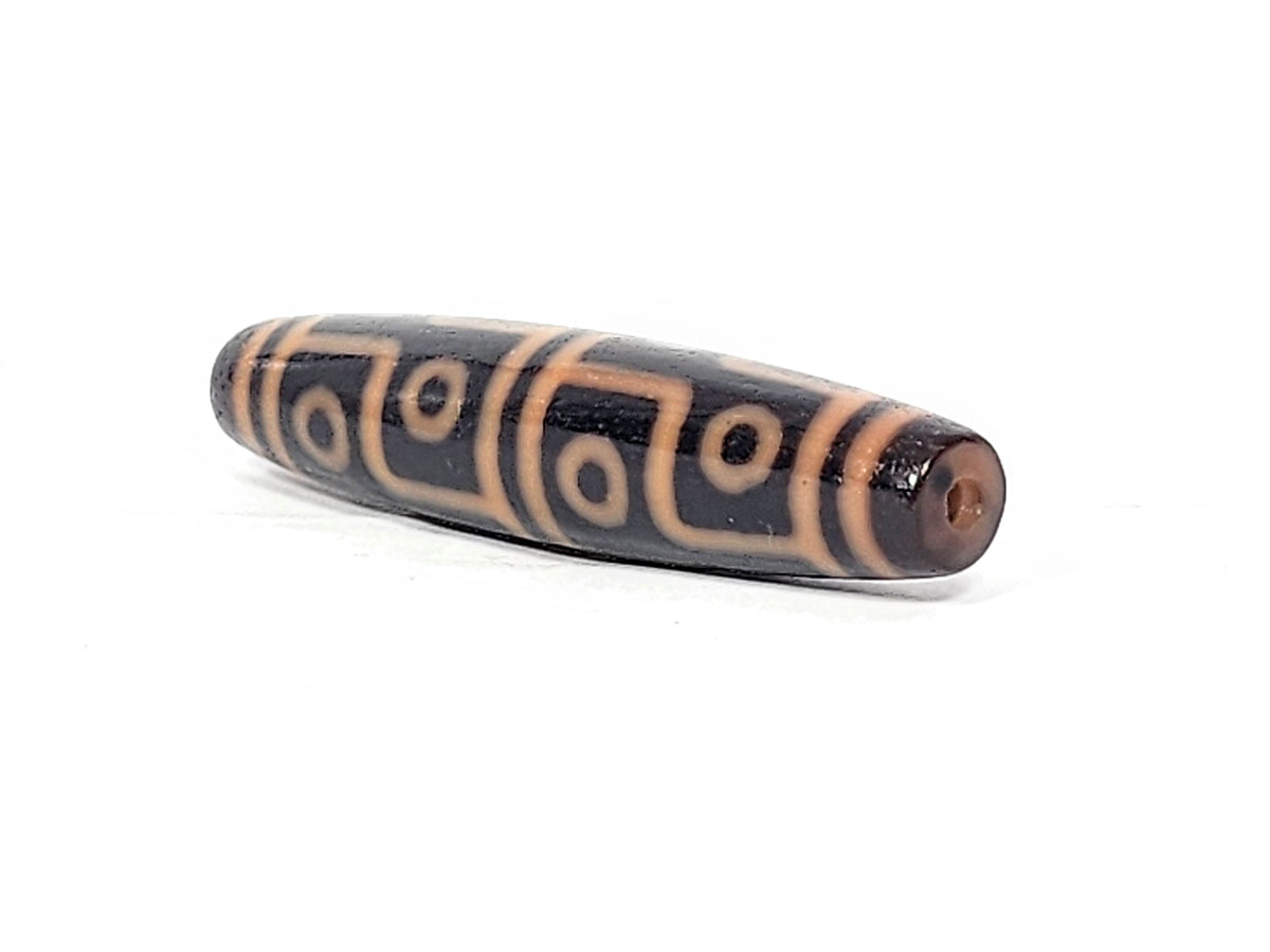 Antique Tibetan 12-eye dzi bead, dark agate with cream eye motifs, geometric lines, visible drill hole, aged patina