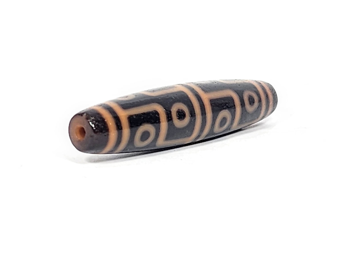 Antique Tibetan 12-eye dzi bead, dark agate, cream eye motifs, visible drill hole, aged patina, elongated barrel shape