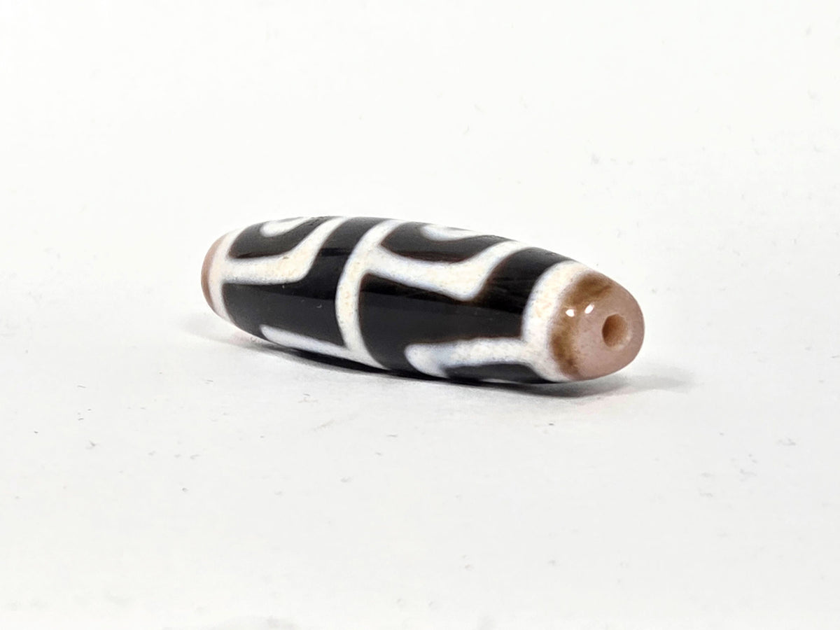 At-042626-4E3 End B, warm sandy-tan end cap, clean drill hole, pitch-black body with white motif, unretouched