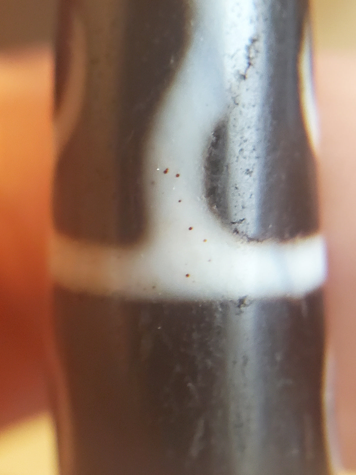 Antique Guru Rinpoche dzi bead close-up showing white motif on dark agate with red bloodspots and aged surface patina