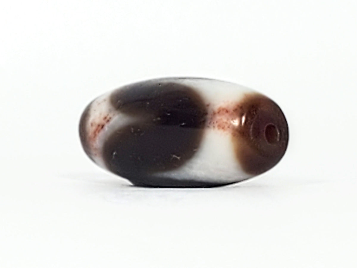 Angled view of antique Tasso dzi At-093024-TaBS3, deep brown agate body, broad cream Tasso wave, bloodspot inclusions, natural weathering marks, 29.4mm × 14.0mm, unretouched