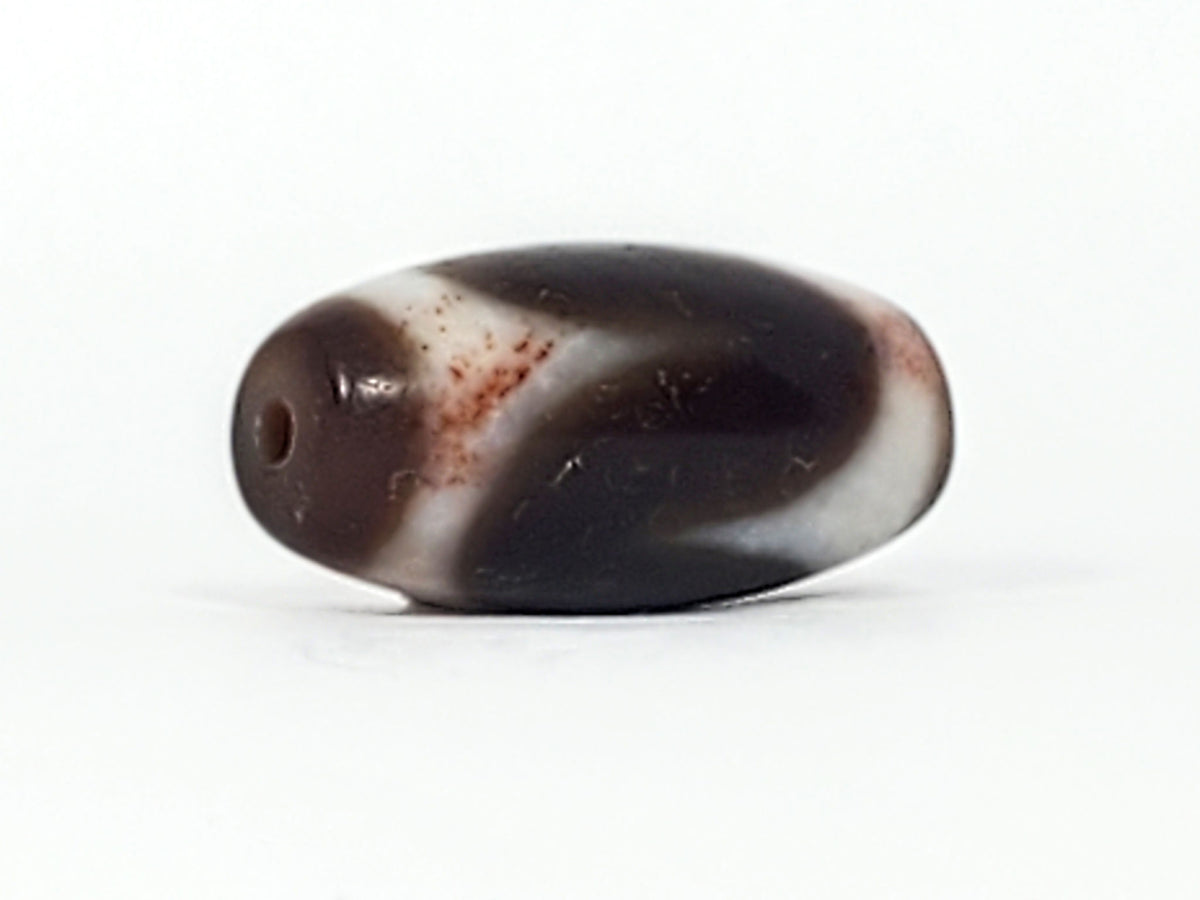 End cap of antique Tasso dzi At-093024-TaBS3, deep brown agate tip with centred drill hole, wide barrel body, cream Tasso zones with bloodspot inclusions visible, unretouched