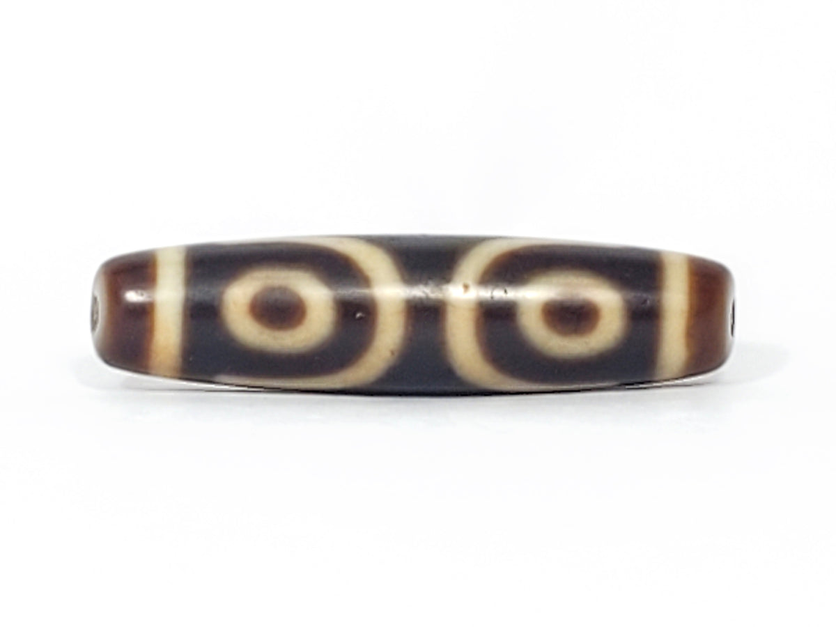 Antique Tibetan three-eye dzi bead, dark agate with cream eye motifs, visible drill holes, aged patina, natural bloodspot markings.