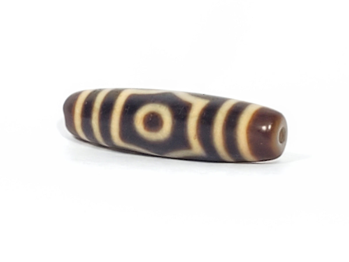 Antique Tibetan dzi bead, three-eye motif, dark brown agate, cream stripe patterning, visible drill hole, natural patina