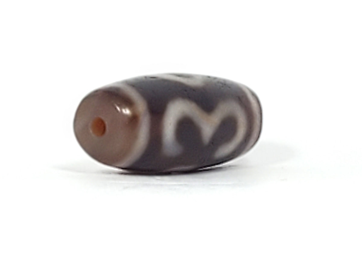 End cap of antique Double Bat Two Eye dzi At-053026-DB2E, dark brown agate tip with centred drill hole, compact barrel body, cream motif visible, bloodspots, unretouched photography