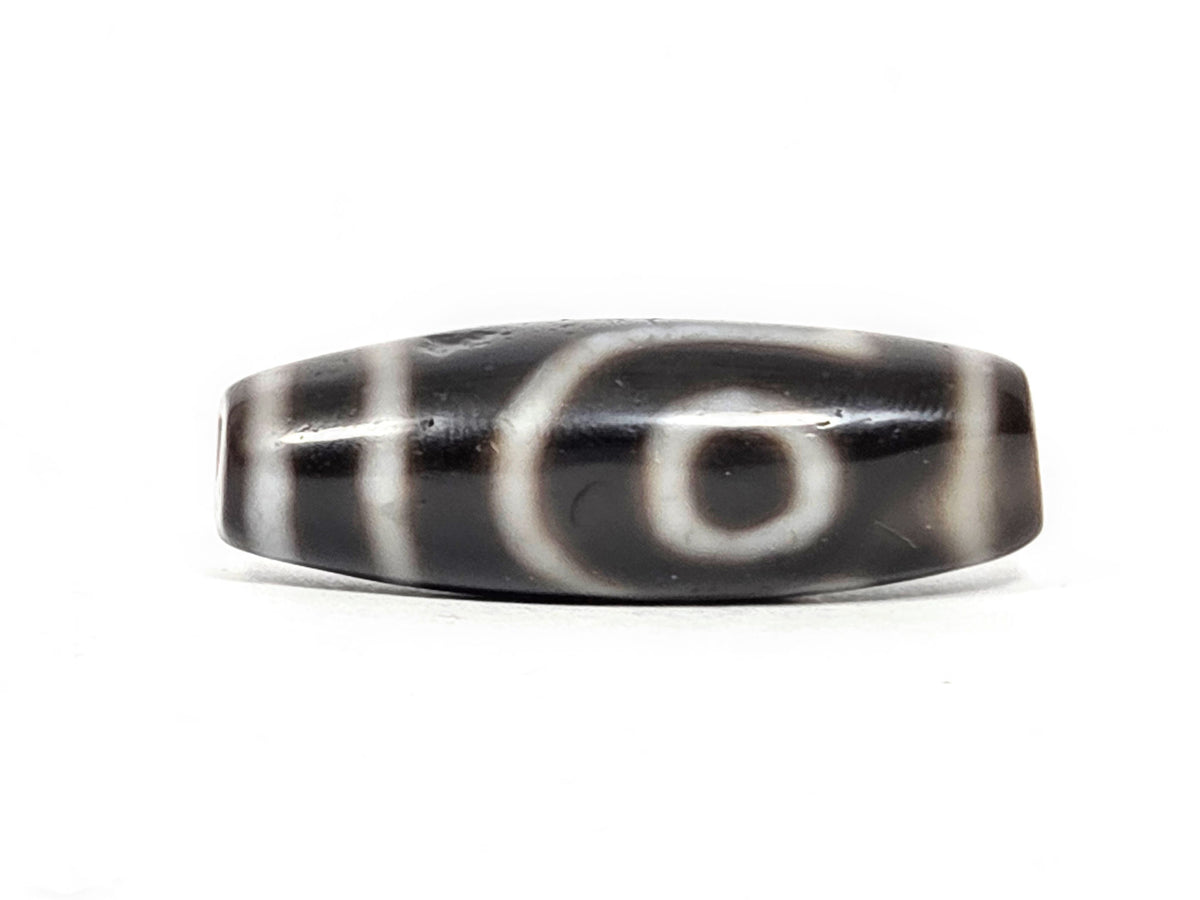 Face B of antique two eye dzi At-033126-2E4, open C-ring eye on pitch-black agate, incomplete outer arc, vertical cream stripes, 37.3mm × 12.8mm, unretouched photography