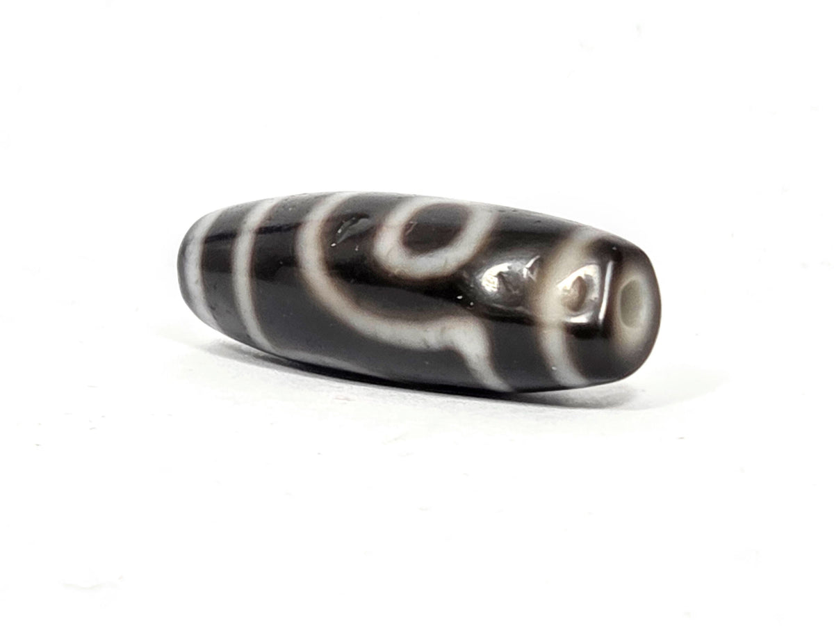 Opposite end cap of antique two eye dzi At-033126-2E4, pitch-black agate tip, cream-ringed drill hole, torpedo body profile, pitch-black throughout, 37.3mm, unretouched