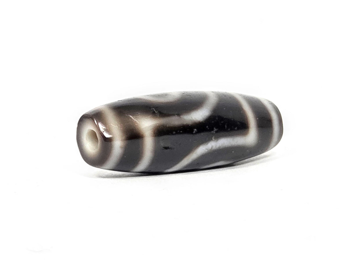 Three-quarter view of antique two eye dzi At-033126-2E4, pitch-black end cap with cream-ringed drill hole, torpedo body, 37.3mm × 12.8mm, unretouched photography
