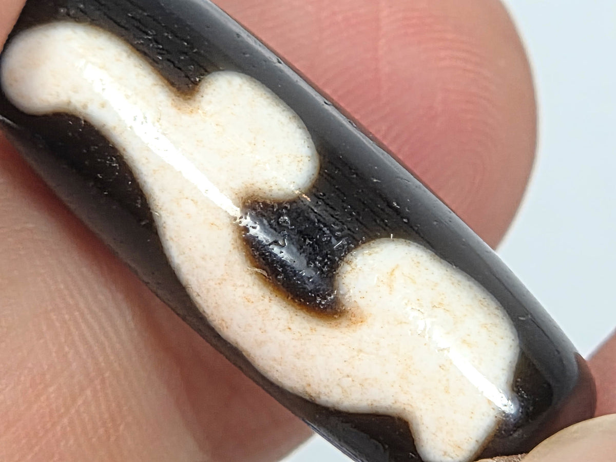 Side angle of vintage dzi bracelet showing the elongated Ruyi bead, cloud-white motif, and mirror-finish black agate beads with gold spacers
