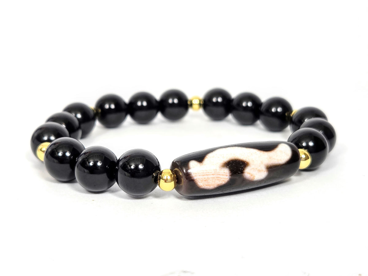 Overhead lifestyle shot of complete black agate and Ruyi dzi bracelet laid flat, unretouched — bloodspot detail visible on the focal bead, Ancient Dzi Shop