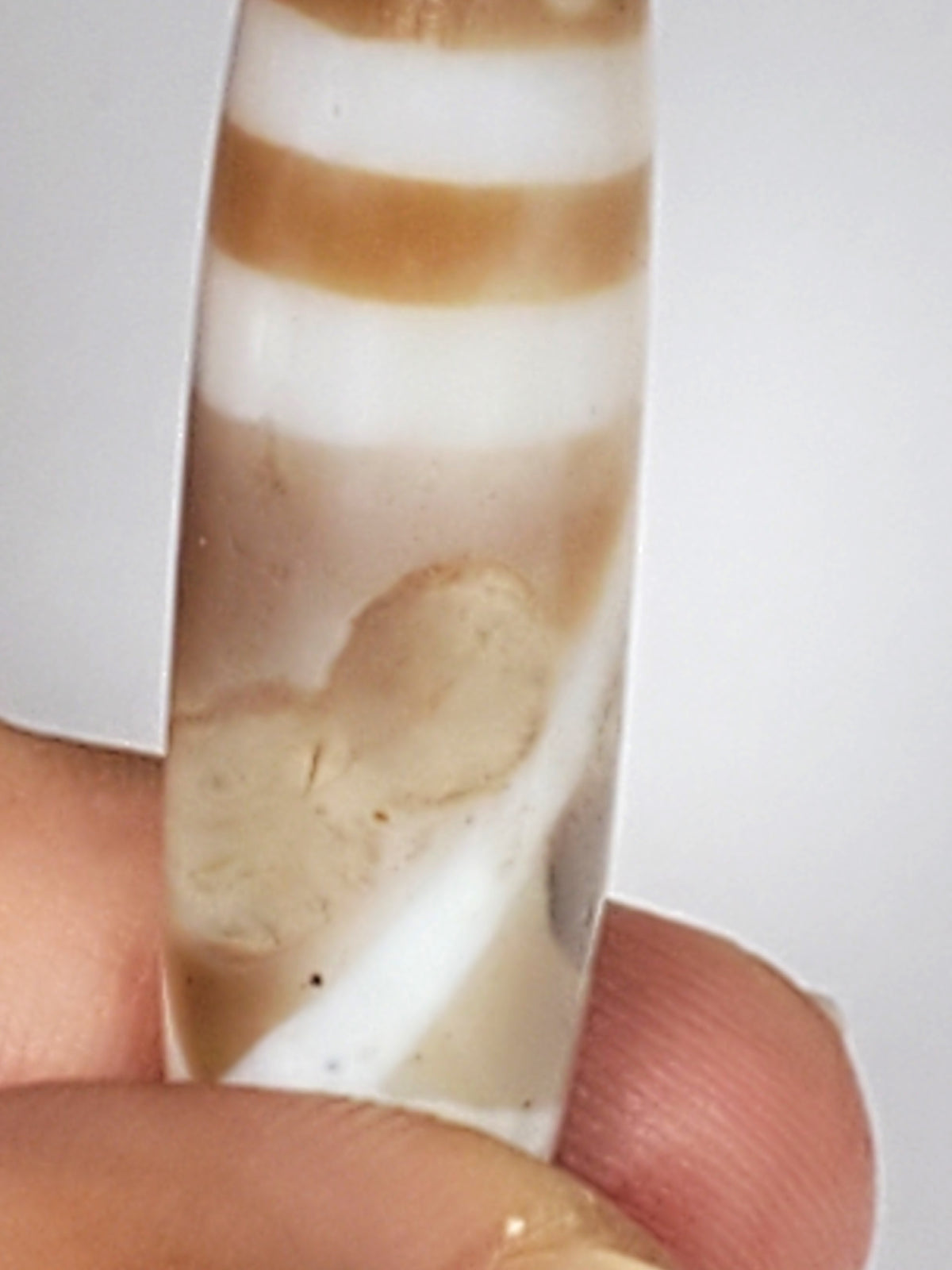 Ancient double mountain motif dzi bead, white agate with tan brown banding, polished cabochon, held between fingers showing natural patina