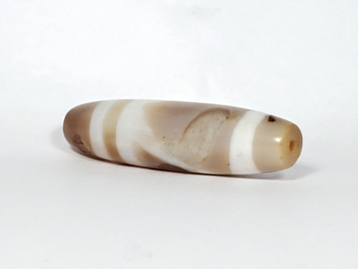 Ancient Tibetan dzi bead, double mountain motif, natural agate, cream brown banding, visible drill hole, aged patina, elongated barrel shape