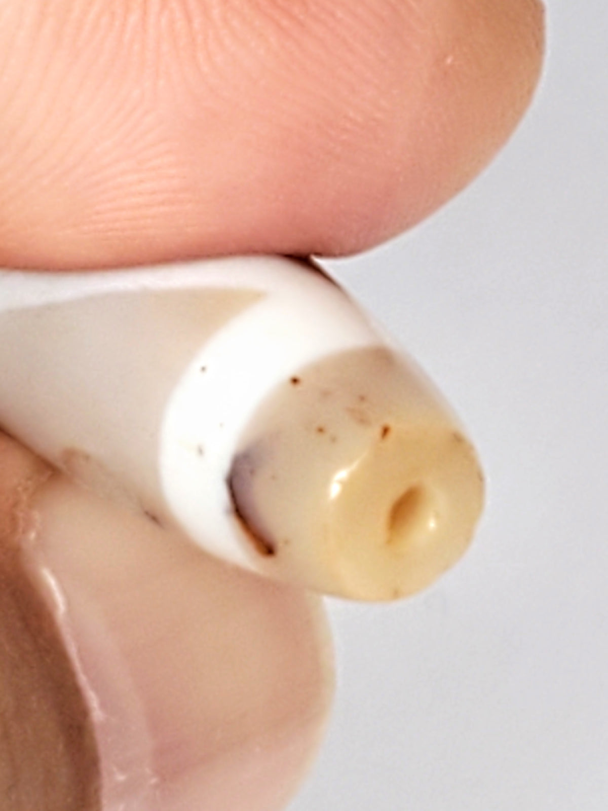 Ancient double mountain motif Tso Dzi bead, creamy agate, visible drill hole, brown bloodspots, aged patina, held by fingers