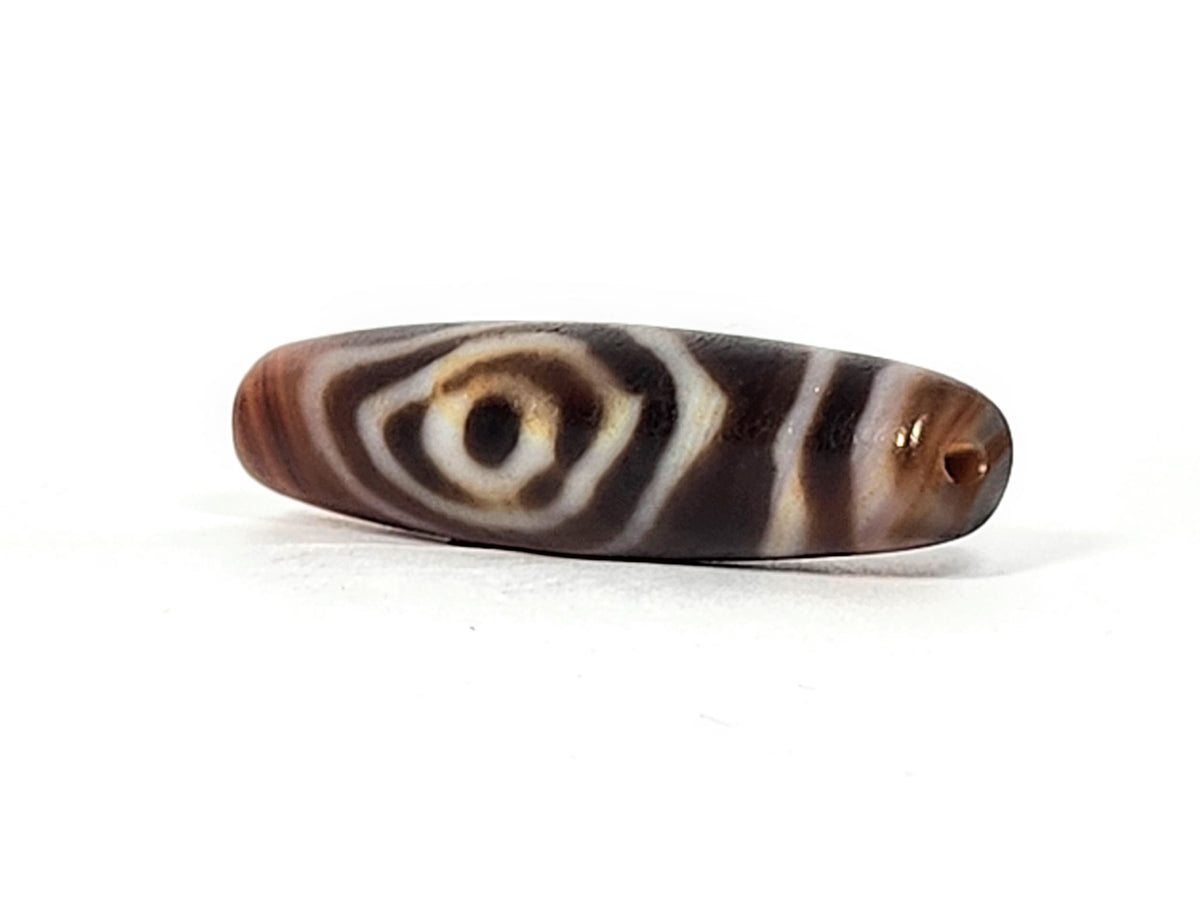 Antique eye-in-eye heaven gate dzi — opposite end, orange-amber drill cap visible at near tip, eye motif on body, At-0426-EIE